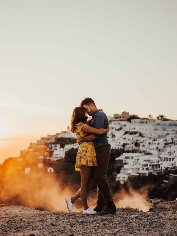 Couple sharing a romantic sunset kiss in Santorini with white-washed buildings glowing golden in the background.