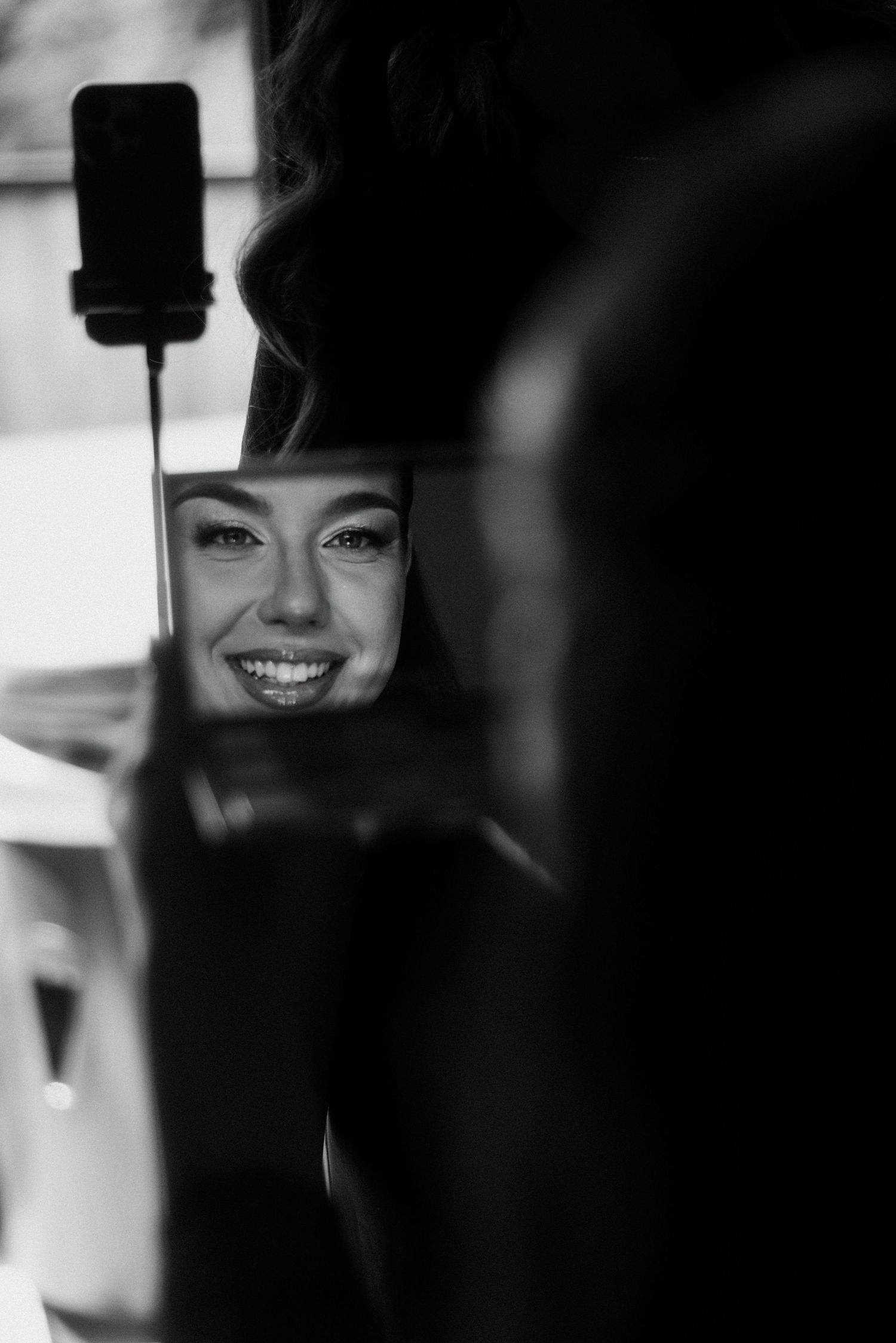Black and white photo of a smiling woman reflected in a car mirror, with curly hair and bright smile.