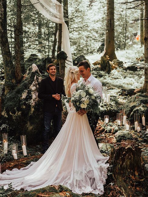 Bride and groom sharing intimate moment at enchanting forest wedding ceremony with candles.