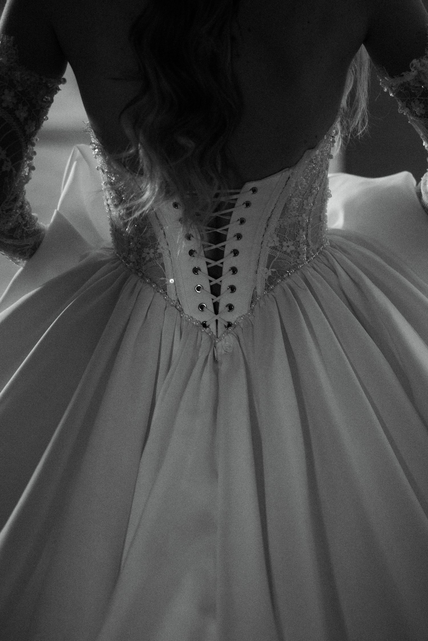 Black and white detail of bridal gown back featuring intricate lace corset with ribbon lacing.