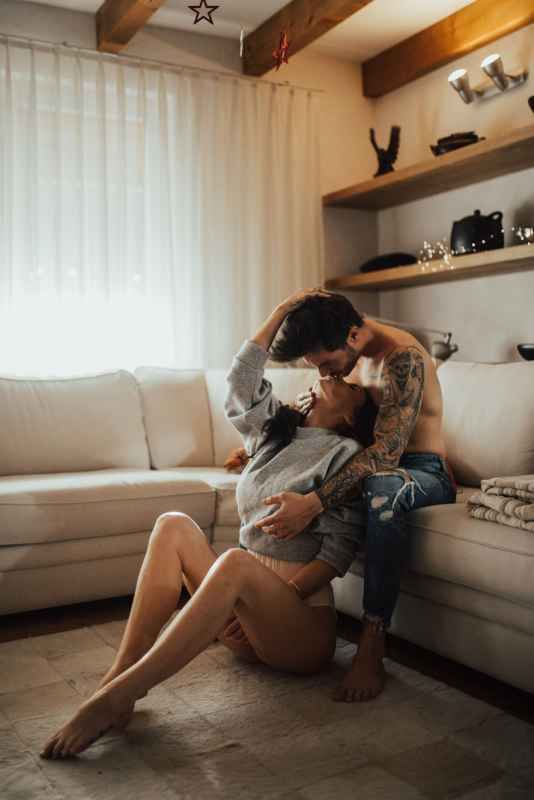 Couple sharing an intimate moment on the floor of a cozy living room with white couch and wooden shelves.