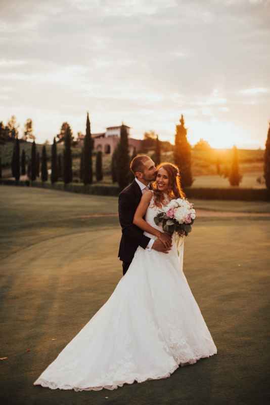 Bride and groom embracing at sunset on a golf course with cypress trees and bouquet.