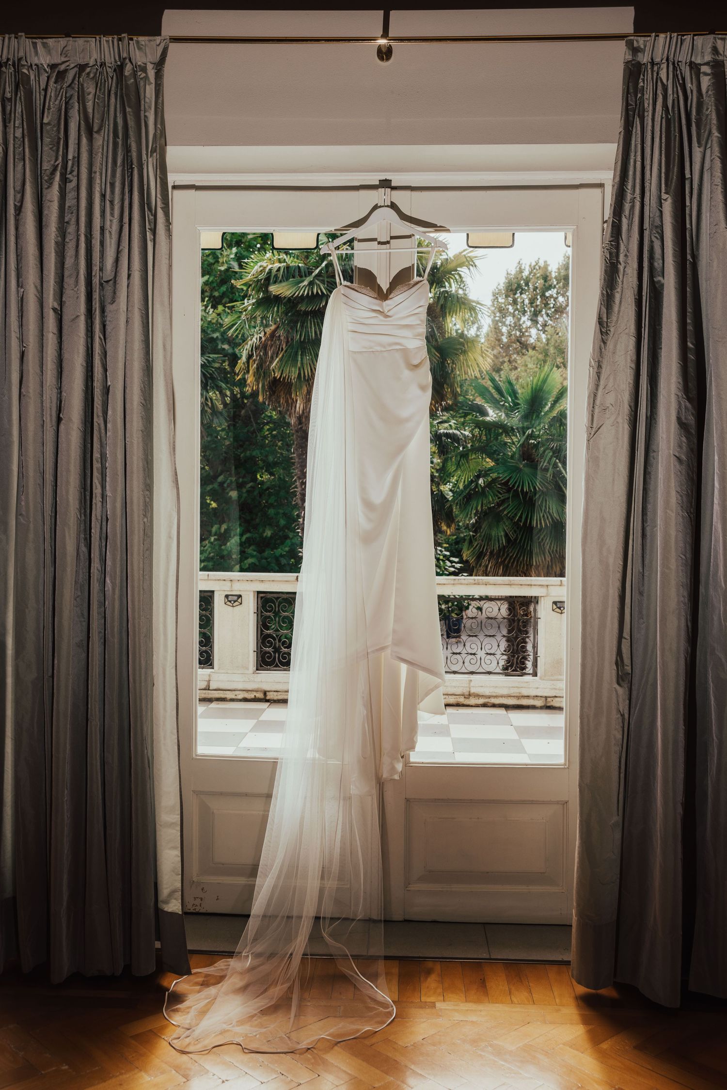 Elegant white wedding dress hanging by window with garden view.