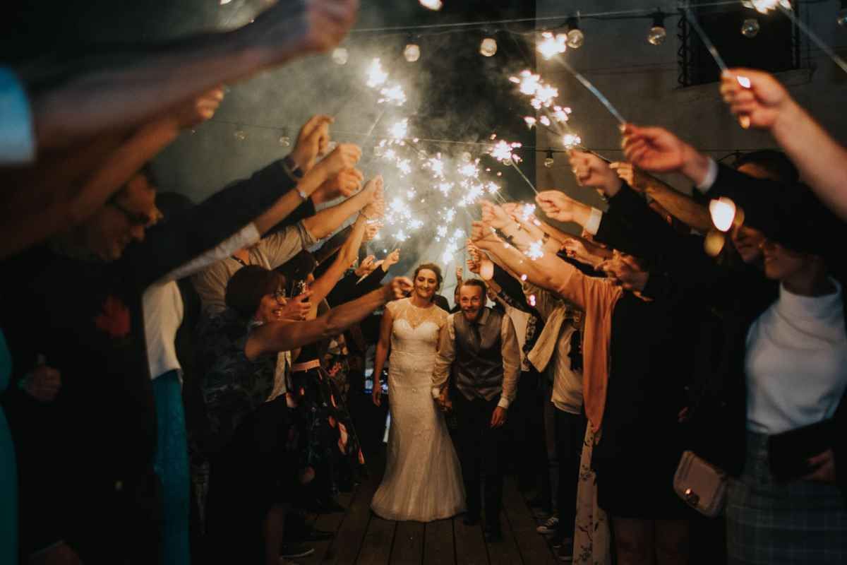 Newlyweds walking through a dazzling sparkler tunnel surrounded by celebrating wedding guests at night.