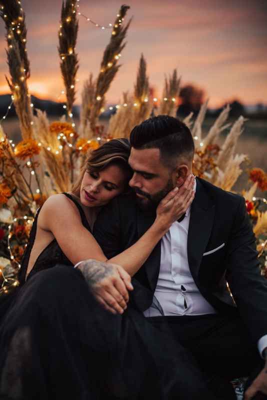 Couple embracing at dusk surrounded by pampas grass and fairy lights.