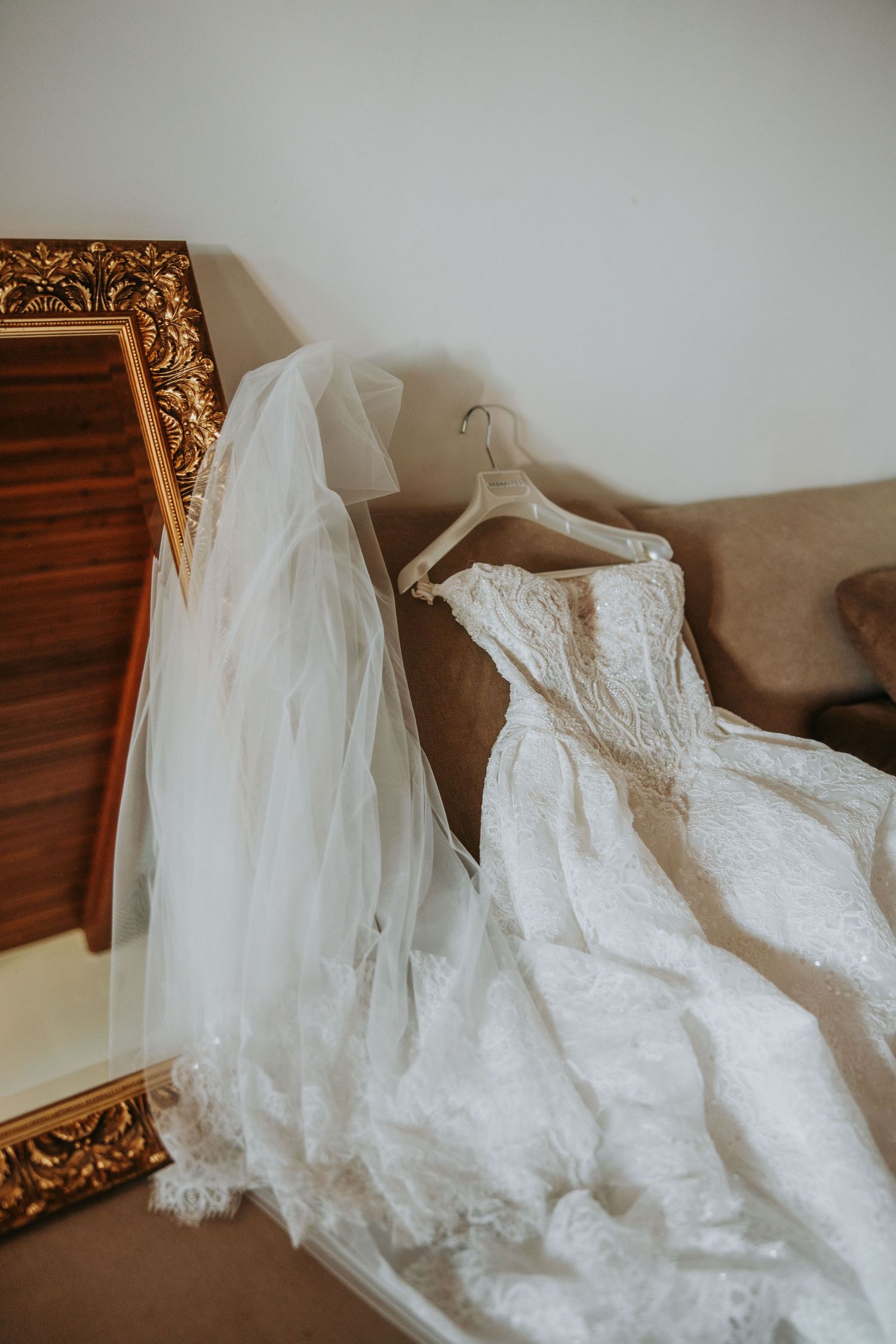 Elegant lace wedding dress and veil draped over a chair next to a gold-framed mirror.