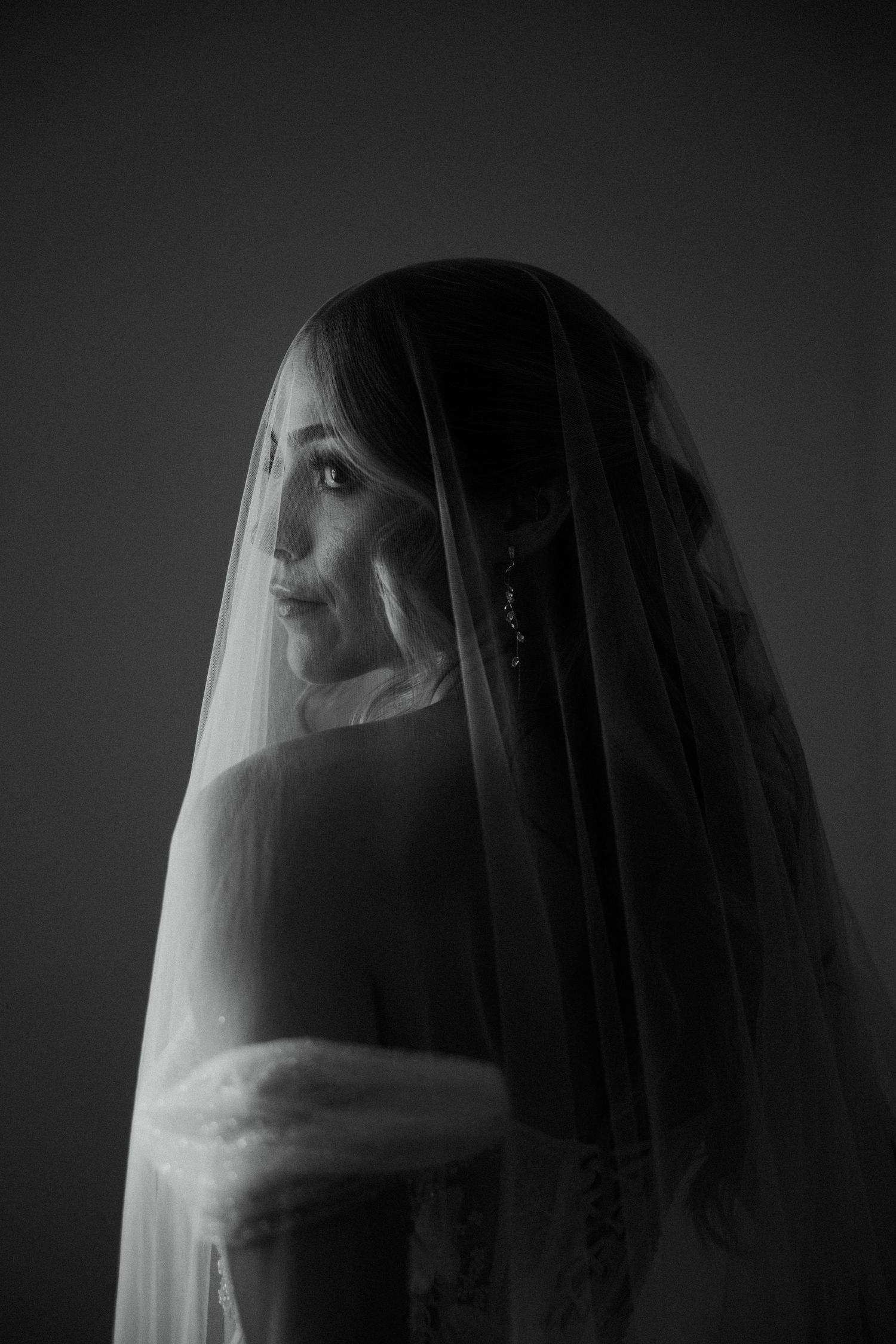 Black and white bridal portrait of a bride wearing a veil, looking over her shoulder with elegant earrings.