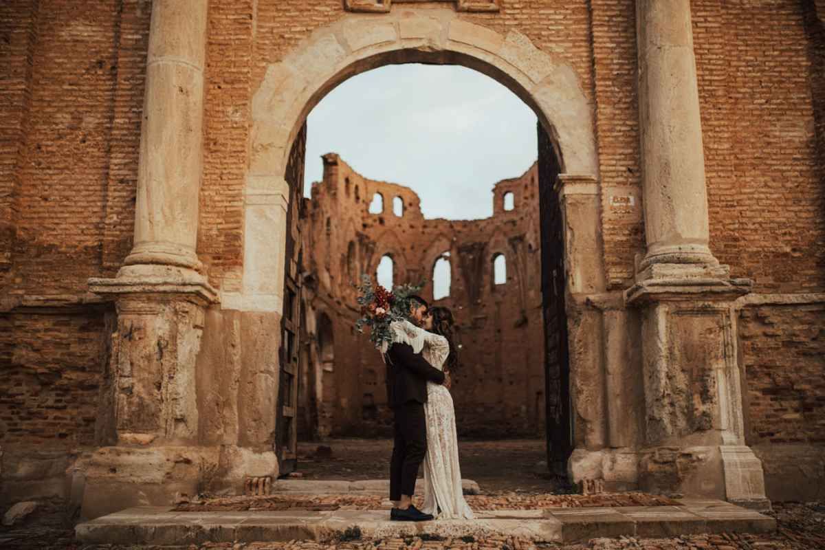 Wedding couple embracing in archway of rustic brick ruins.