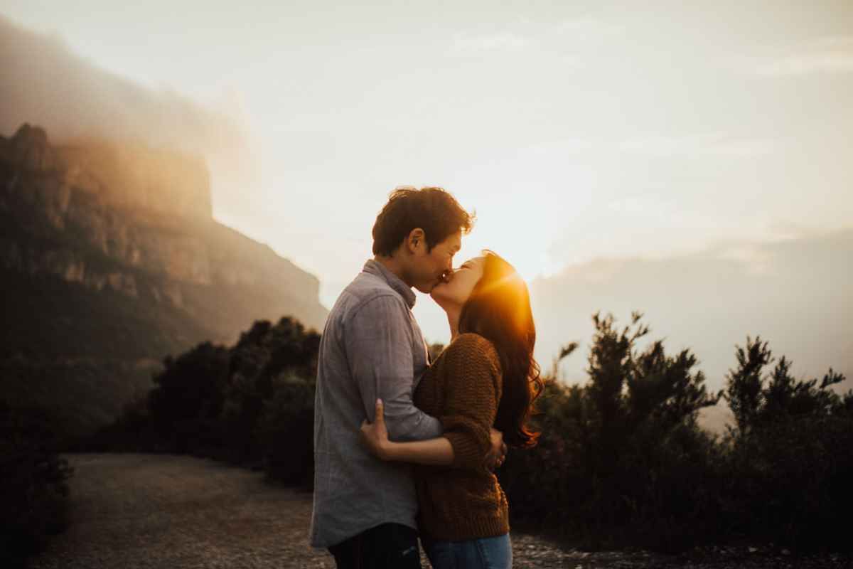 Couple sharing a romantic almost-kiss at golden sunset with misty mountains in the background.