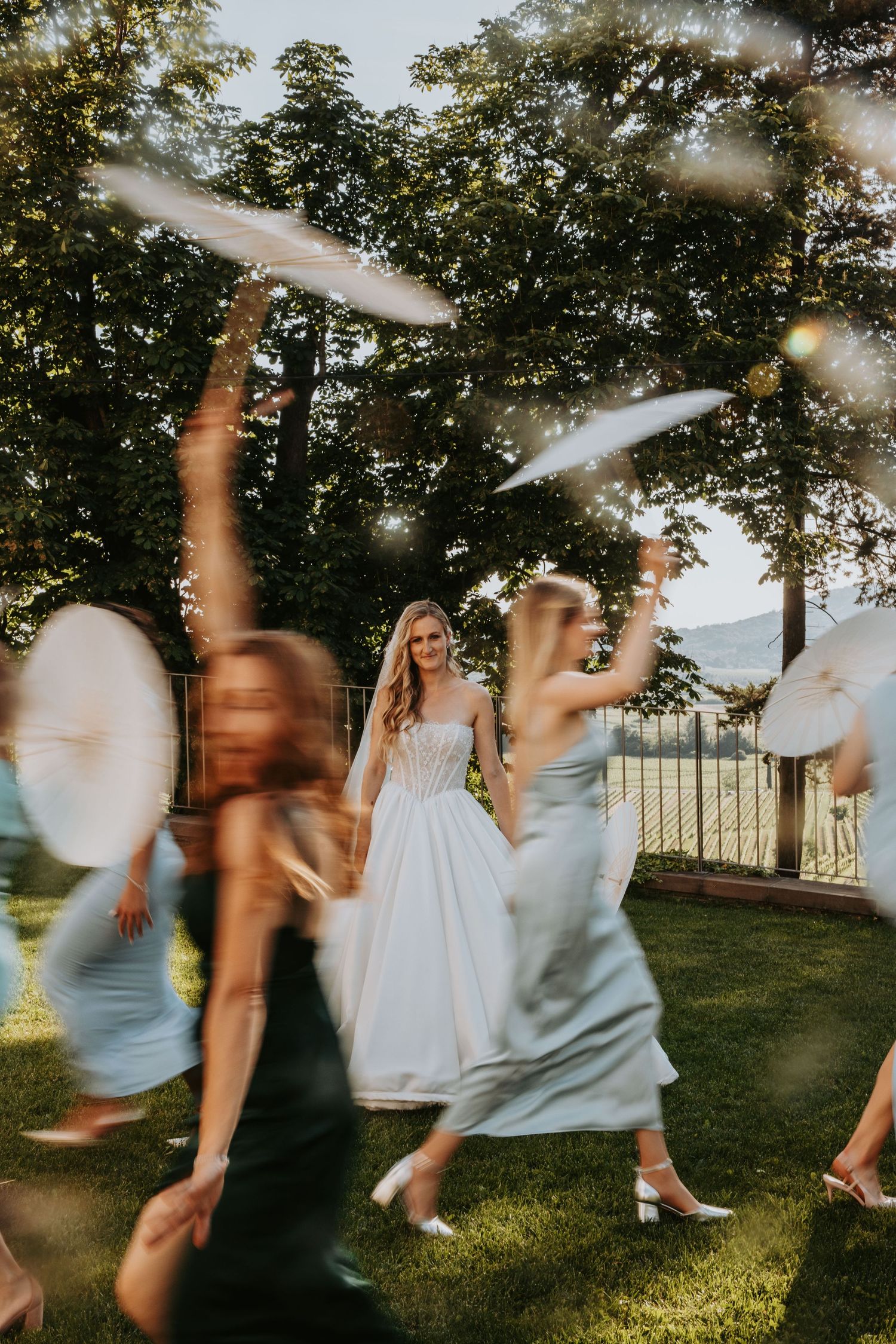 Bride in white gown surrounded by bridesmaids in blue dresses dancing outdoors with motion blur effect.