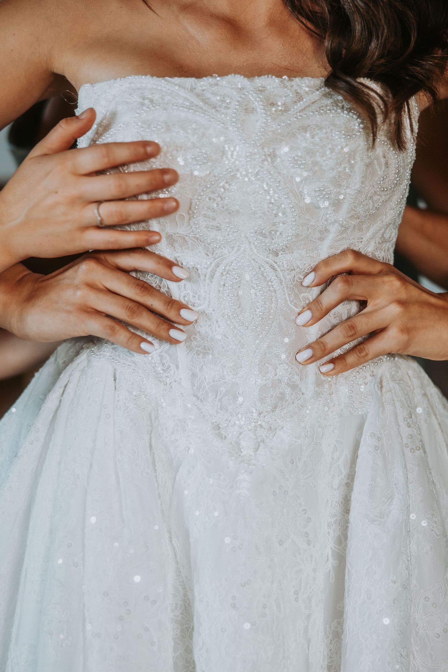 Close-up of a bride in a white lace strapless wedding gown with hands placed on her waist.