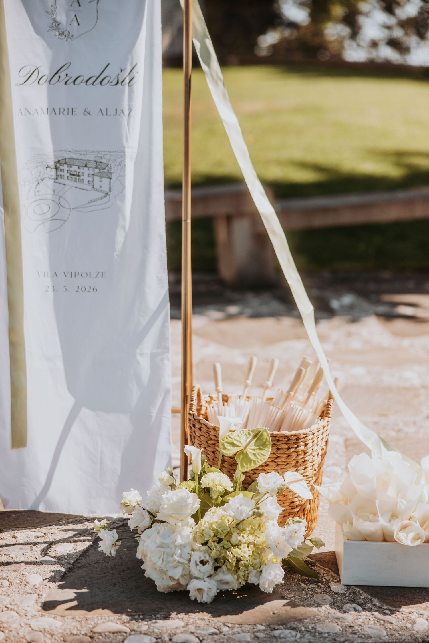 White wedding welcome sign with floral bouquet and wicker basket with programs on stone patio.