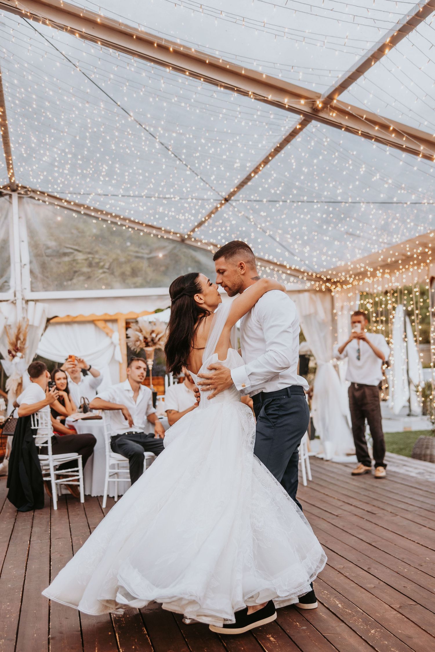 Bride and groom sharing first dance under fairy lights in elegant wedding tent.
