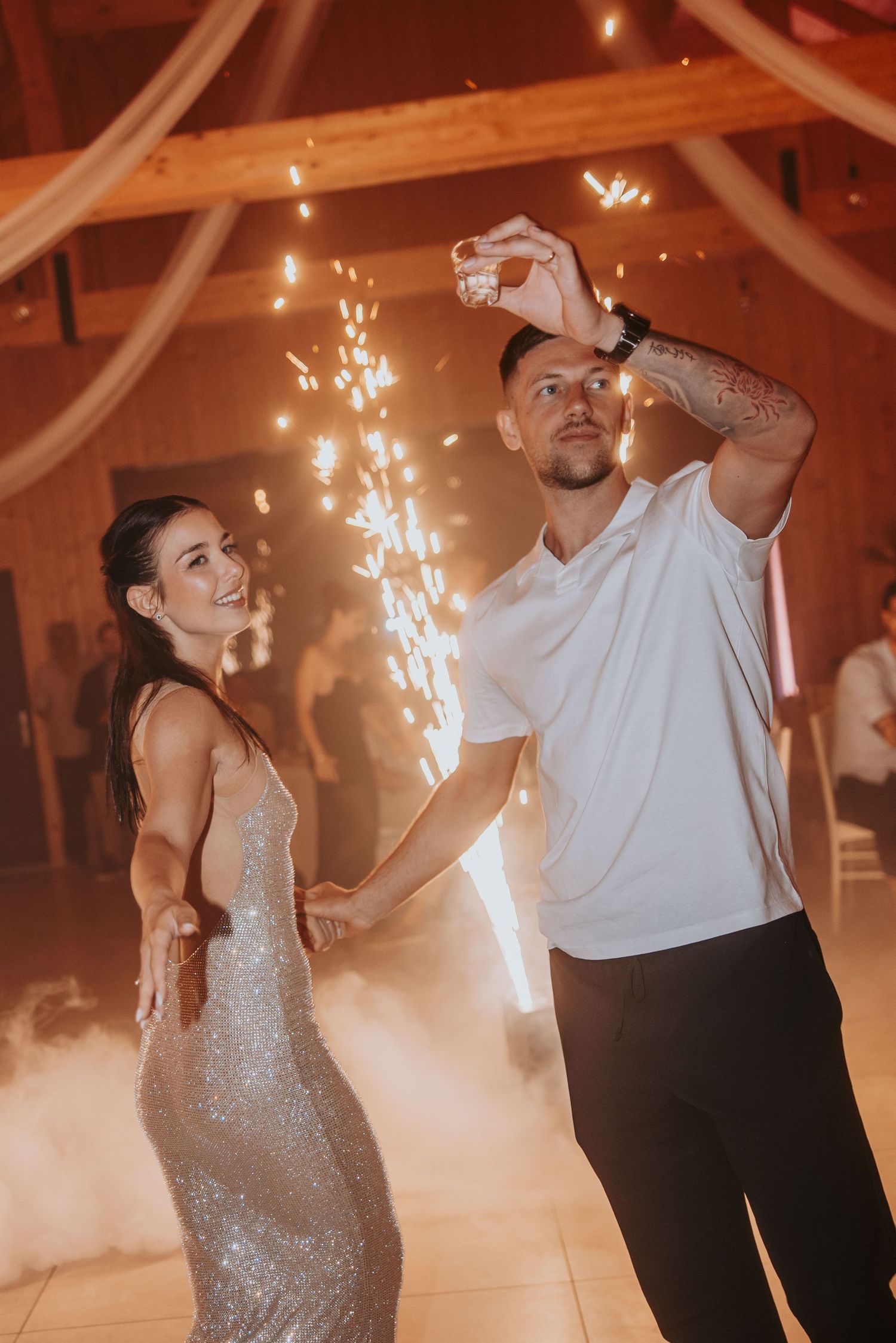 Couple dances together on foggy wedding reception dance floor with fireworks and warm string lights.