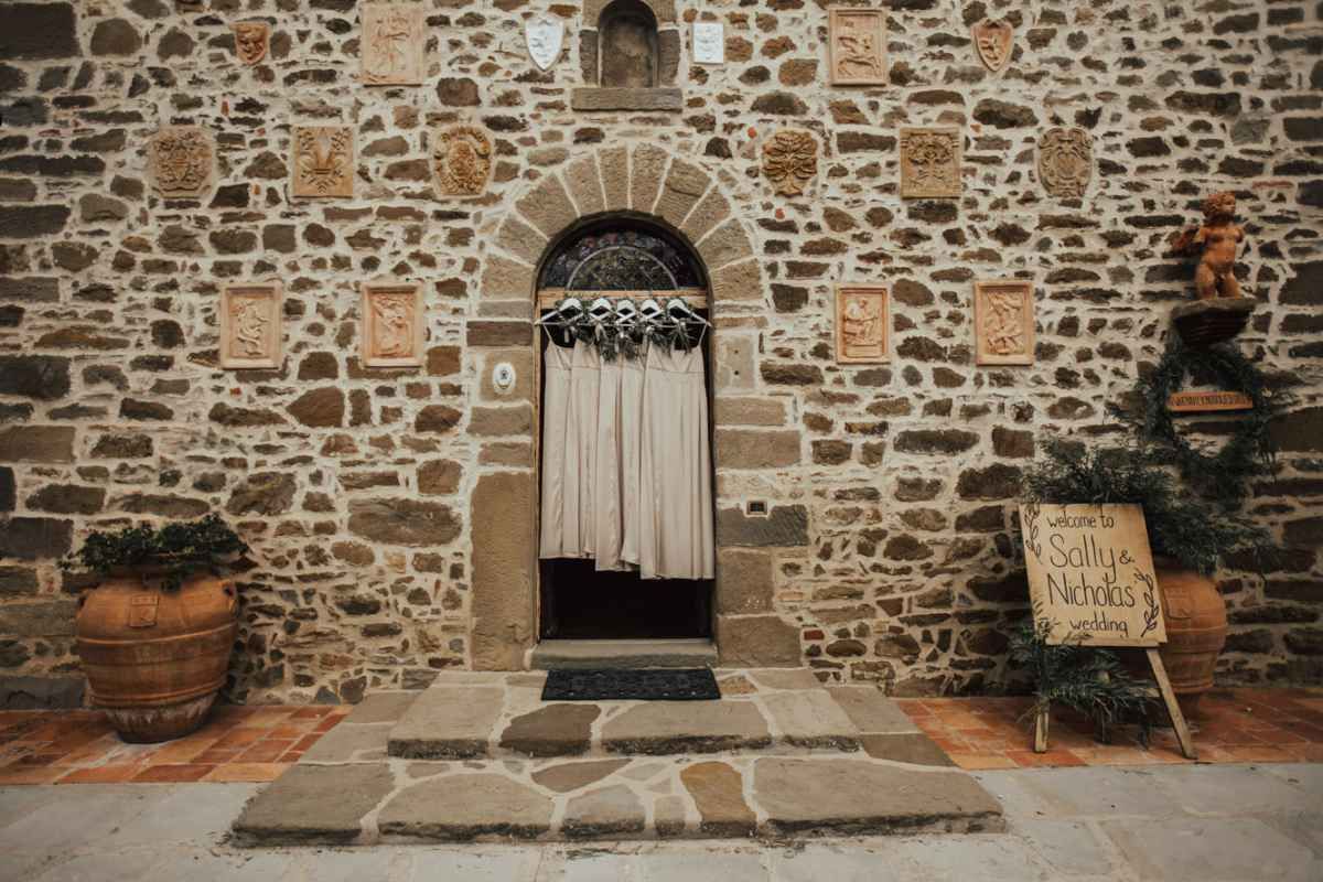 Rustic stone wall building with arched wooden door decorated with hanging fabric and terracotta pots in Tuscany.