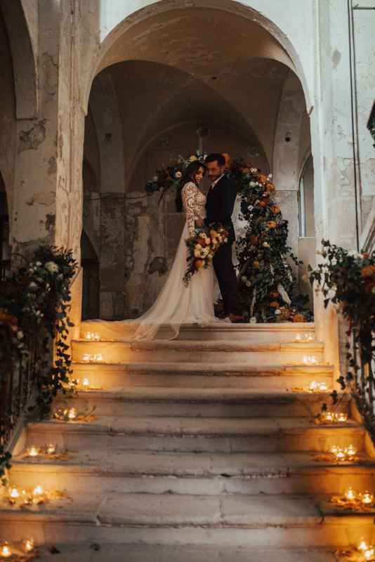 Elegant bride and groom kissing on candlelit stone steps in a rustic church.