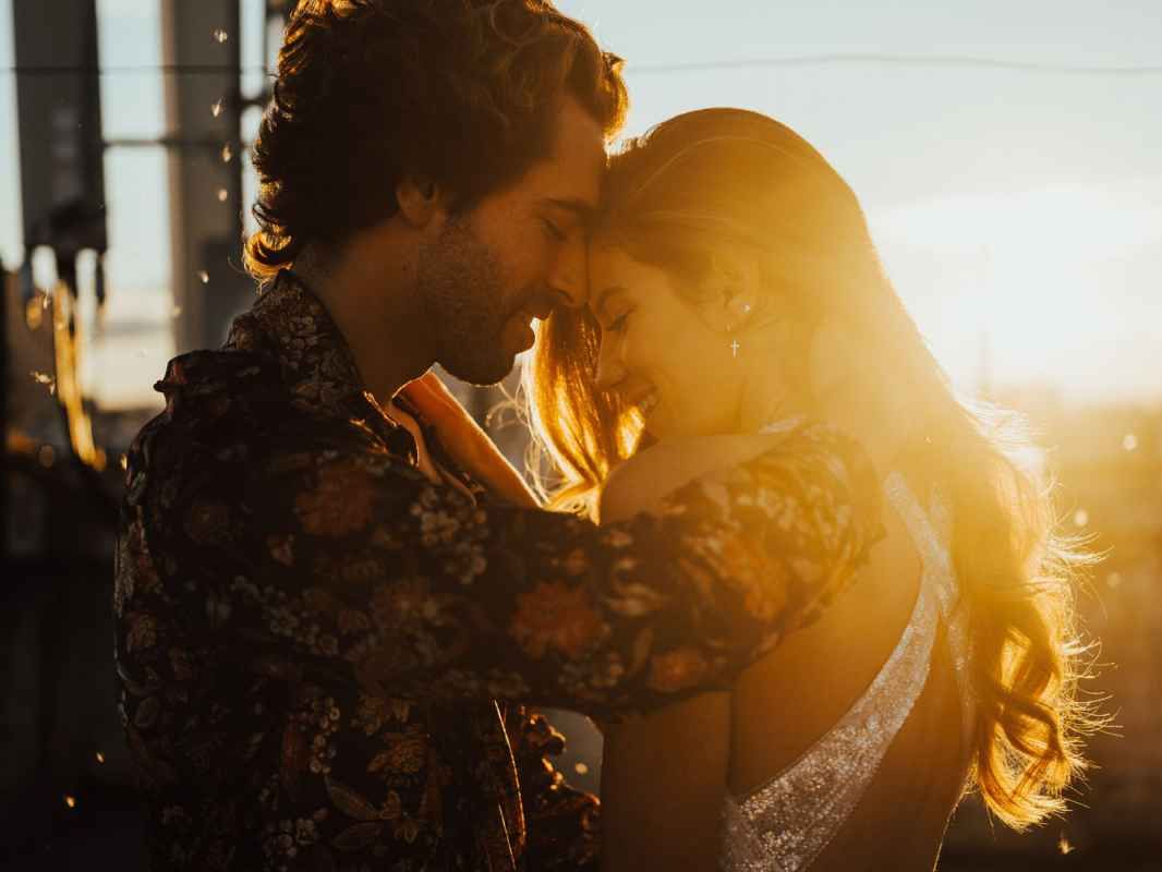 Romantic couple nearly kissing bathed in golden sunset light outdoors.