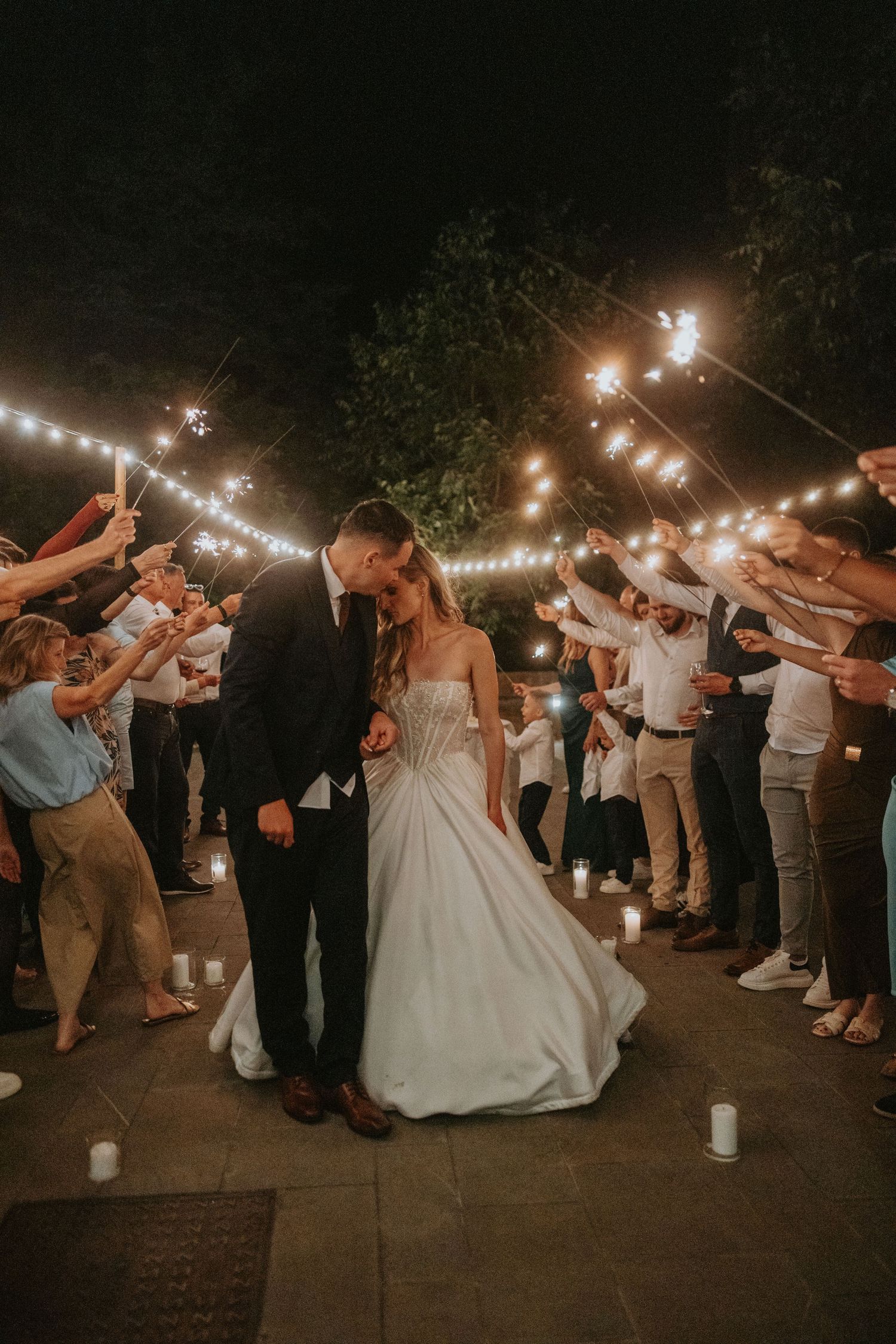 Bride and groom share a kiss during magical sparkler exit at outdoor nighttime wedding reception.