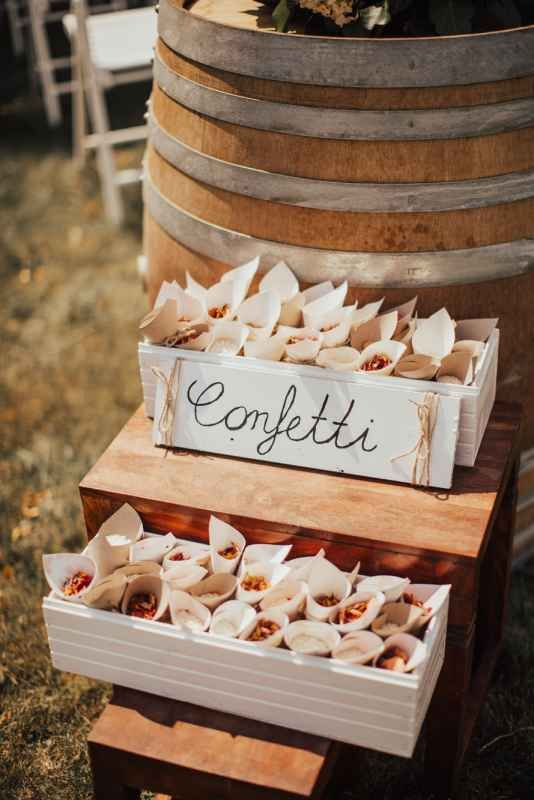 Rustic wedding confetti cones displayed in wooden boxes on a barrel for outdoor ceremony.