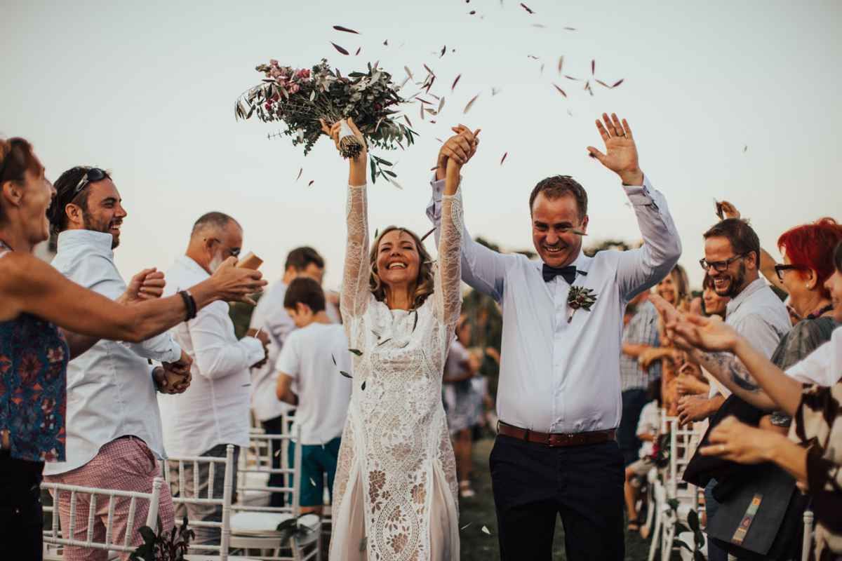 Joyful bride and groom walk down aisle as guests celebrate with confetti outdoors.