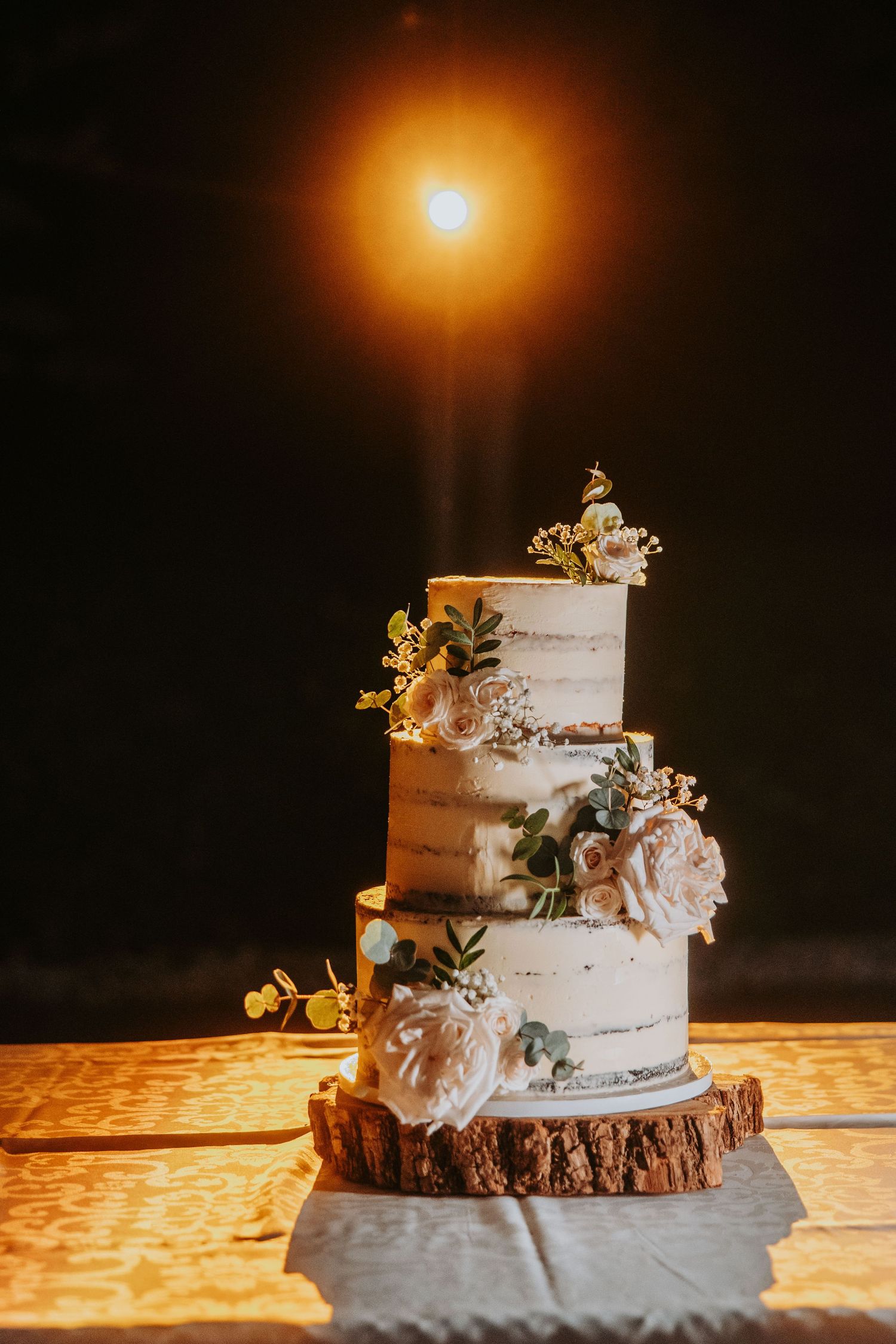 Elegant three-tier semi-naked wedding cake decorated with blush roses on rustic wood slice stand.