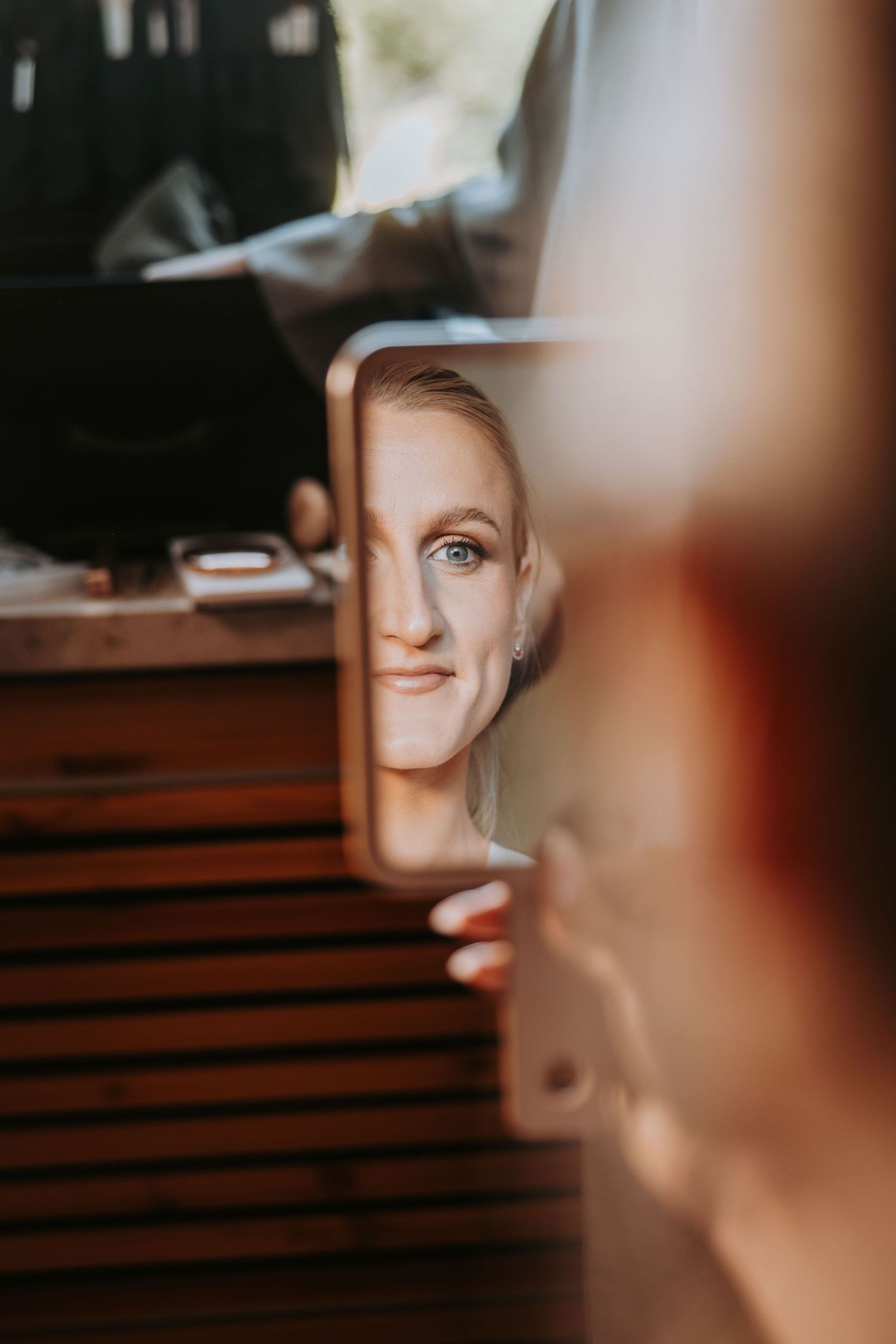 Bride smiling at her reflection in a small mirror during wedding preparations.