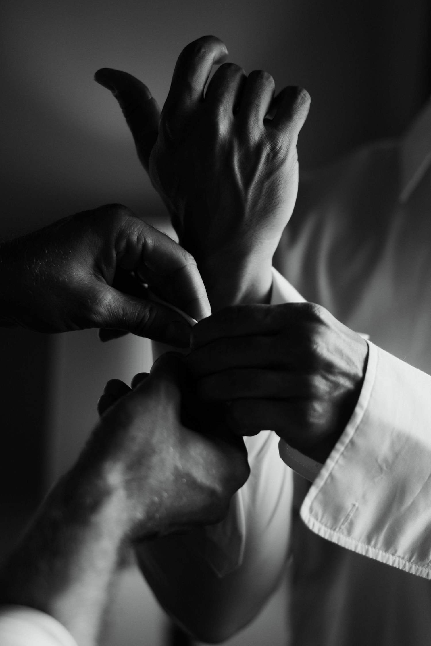 Black and white photo of hands fastening a cufflink on a white dress shirt sleeve.