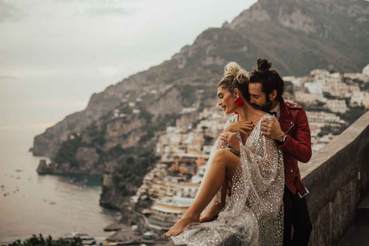 Bride and groom standing on a terrace overlooking the stunning coastal town of Positano, Italy.