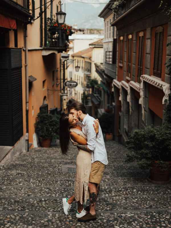Couple embracing romantically on a cobblestone street in a charming Italian village with colorful buildings.