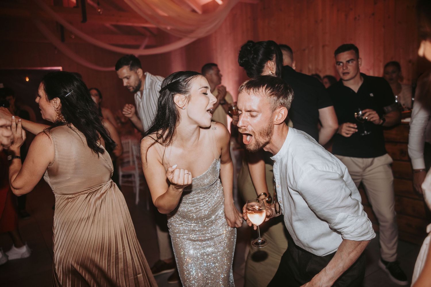 Bride and groom dancing energetically with guests at a lively wedding reception party.