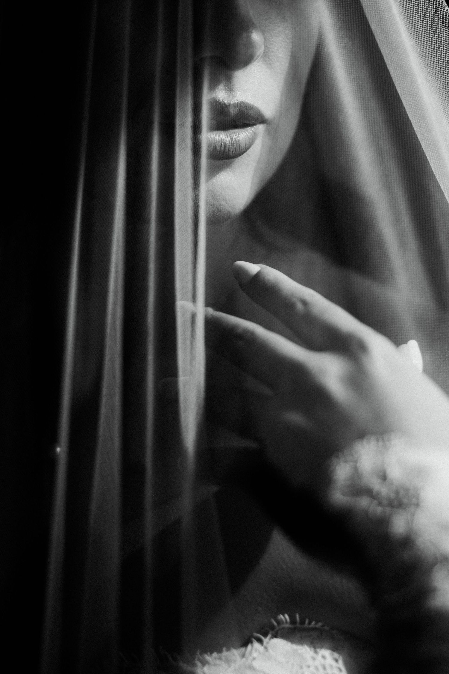 A black and white artistic bridal portrait showing a bride partially veiled, with soft light highlighting her features.