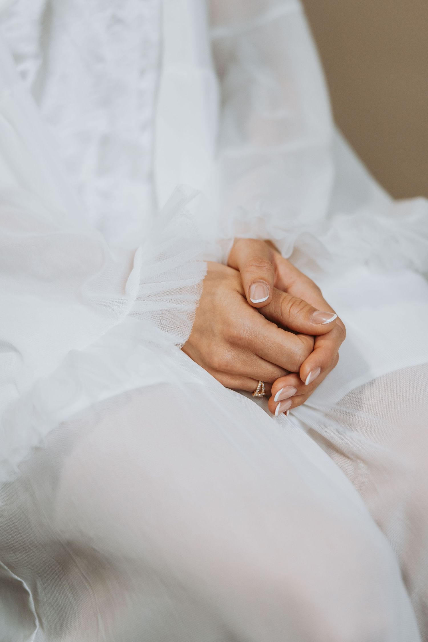 Close-up of a bride's hands clasped together wearing an engagement ring over a white tulle wedding dress.