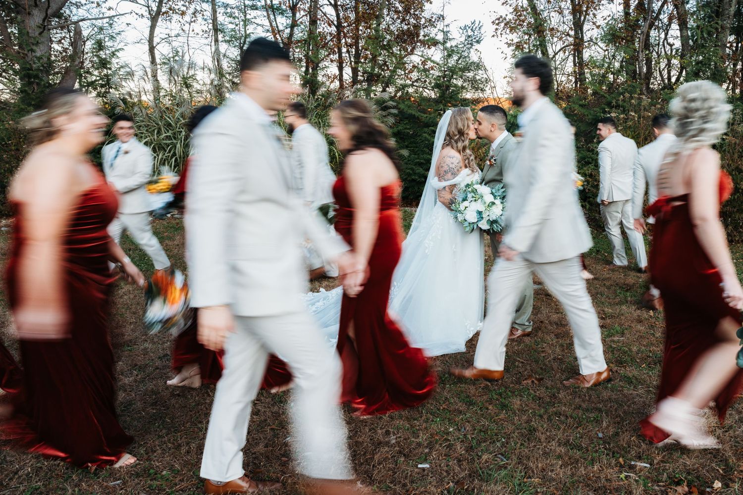 Wedding party walking through a wooded area, bridesmaids in burgundy dresses and groomsmen in gray suits.