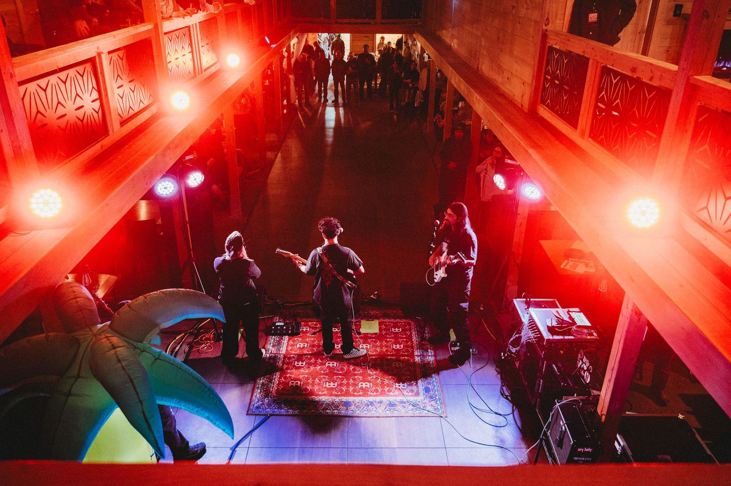 Live band performing on stage bathed in red lighting inside an ornate venue, viewed from above.