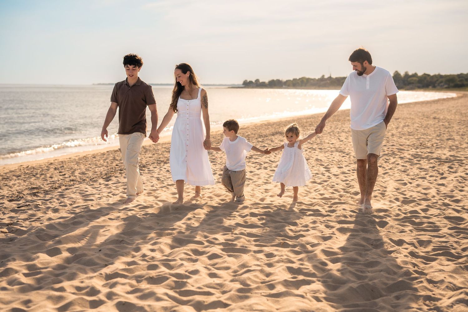 Family of five walking hand-in-hand on a sandy beach at golden hour sunset.