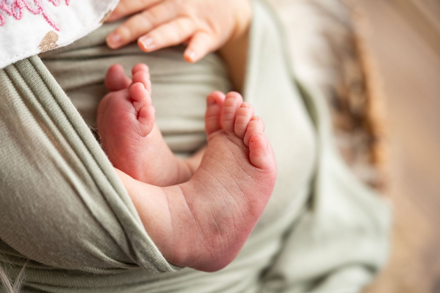 Close-up of tiny newborn baby feet peeking out from a soft sage green swaddle wrap.