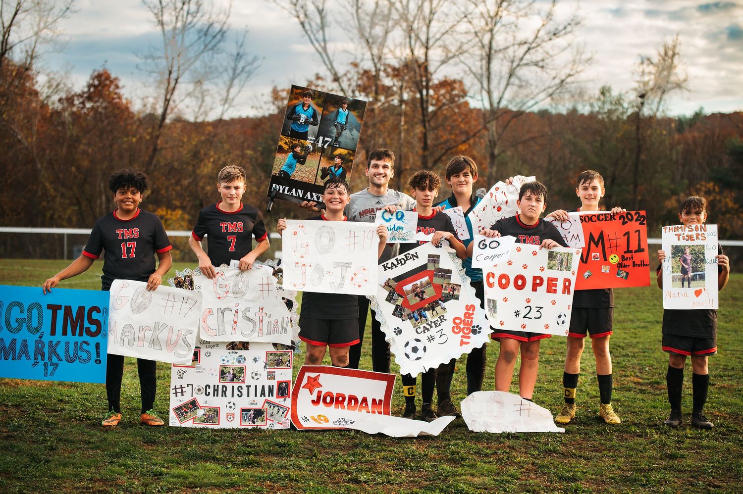 Youth soccer players holding personalized fan signs and posters on a grass field during a team celebration event.