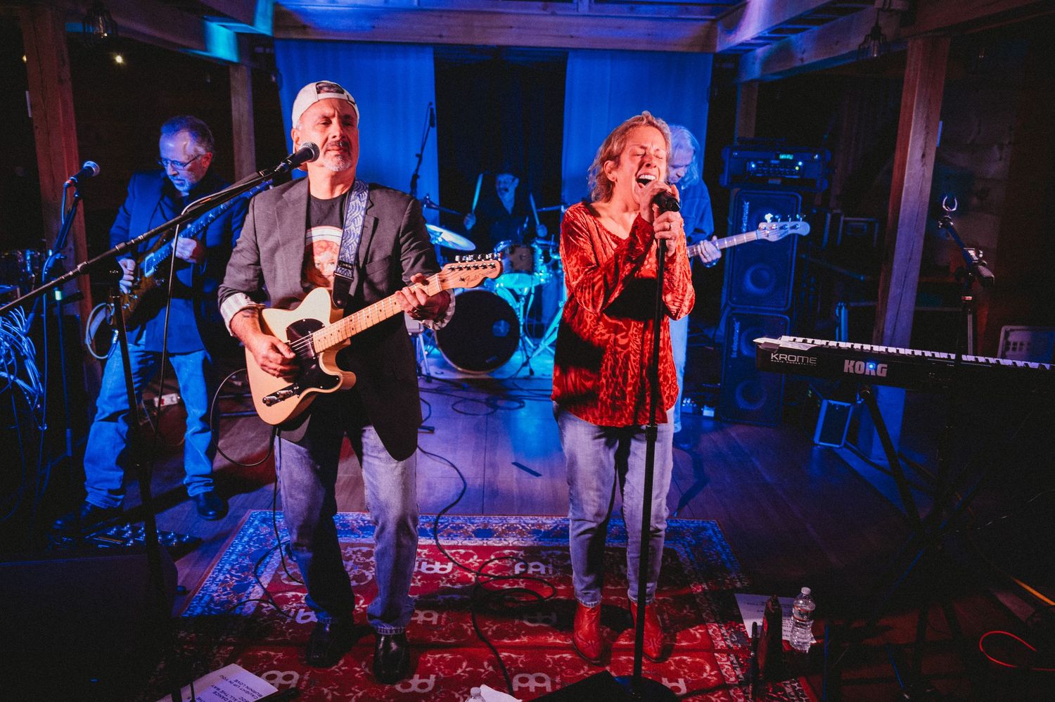 Live band performance with male guitarist and female vocalist singing on stage under blue and purple lights.