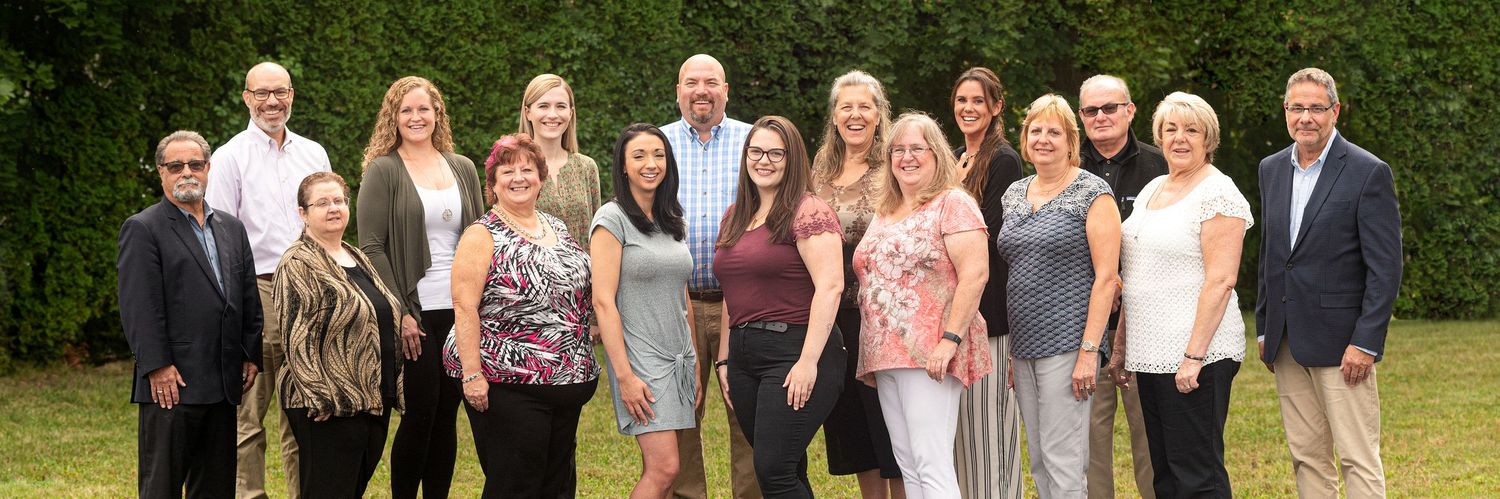A professional group of real estate team members posing outdoors in a lush garden setting for a team photo.