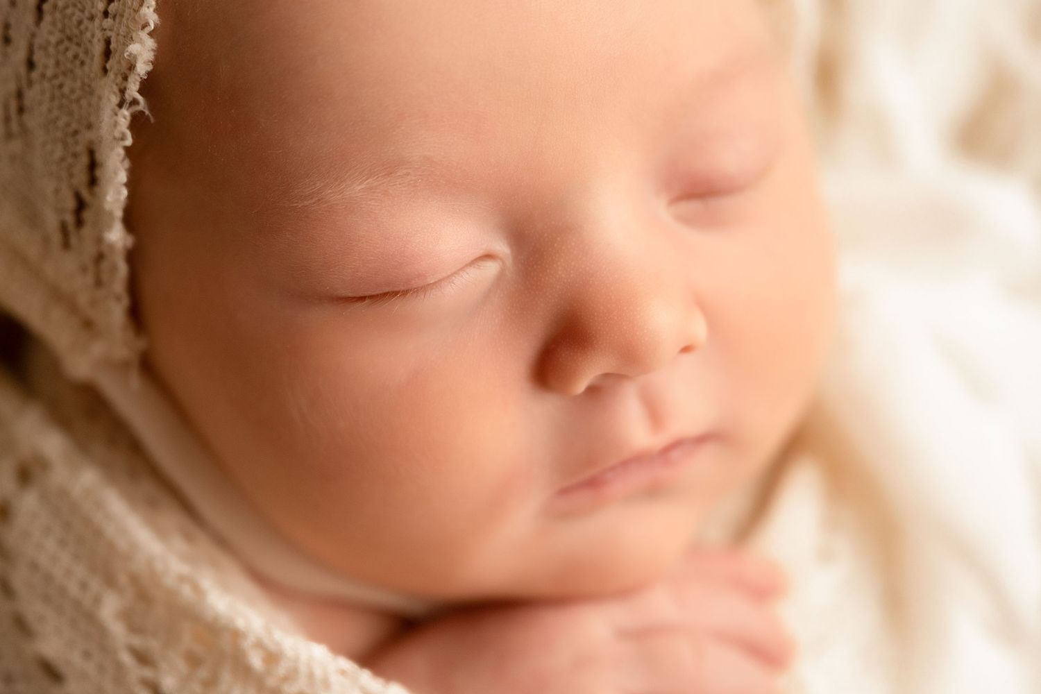 Close-up of a peaceful sleeping newborn baby with soft skin, tiny hands, and a cream knit wrap.