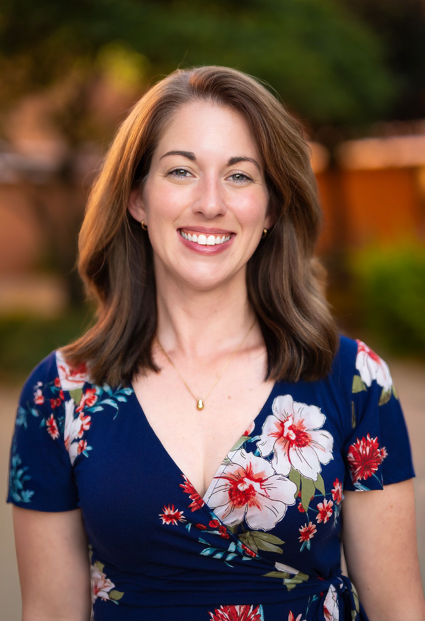 Smiling woman in blue floral wrap dress poses for professional outdoor headshot portrait.