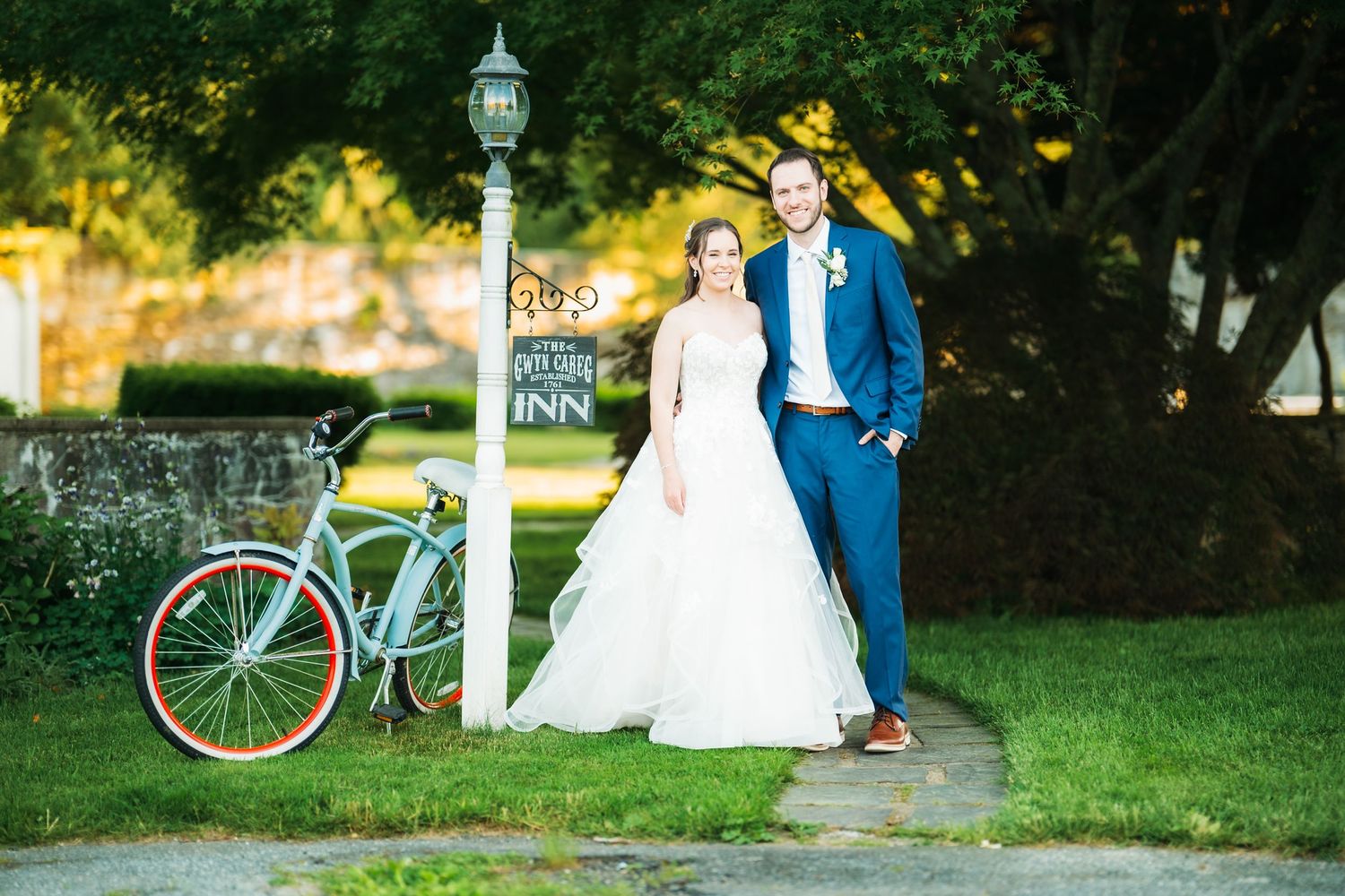 Bride and groom pose by a lamppost near a teal bicycle at an inn on their wedding day.