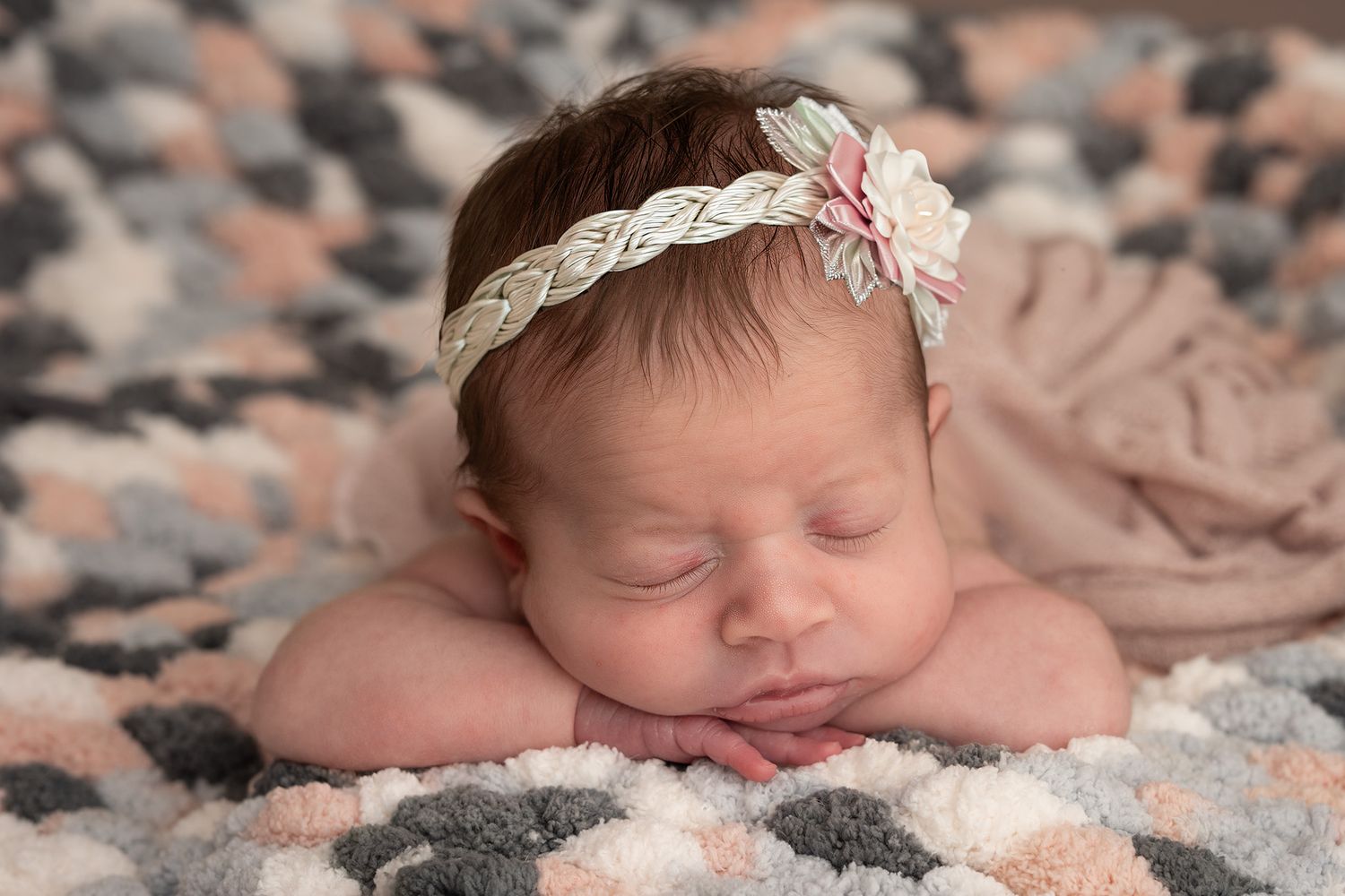 Newborn baby girl sleeping peacefully on a colorful blanket wearing a delicate floral lace headband.