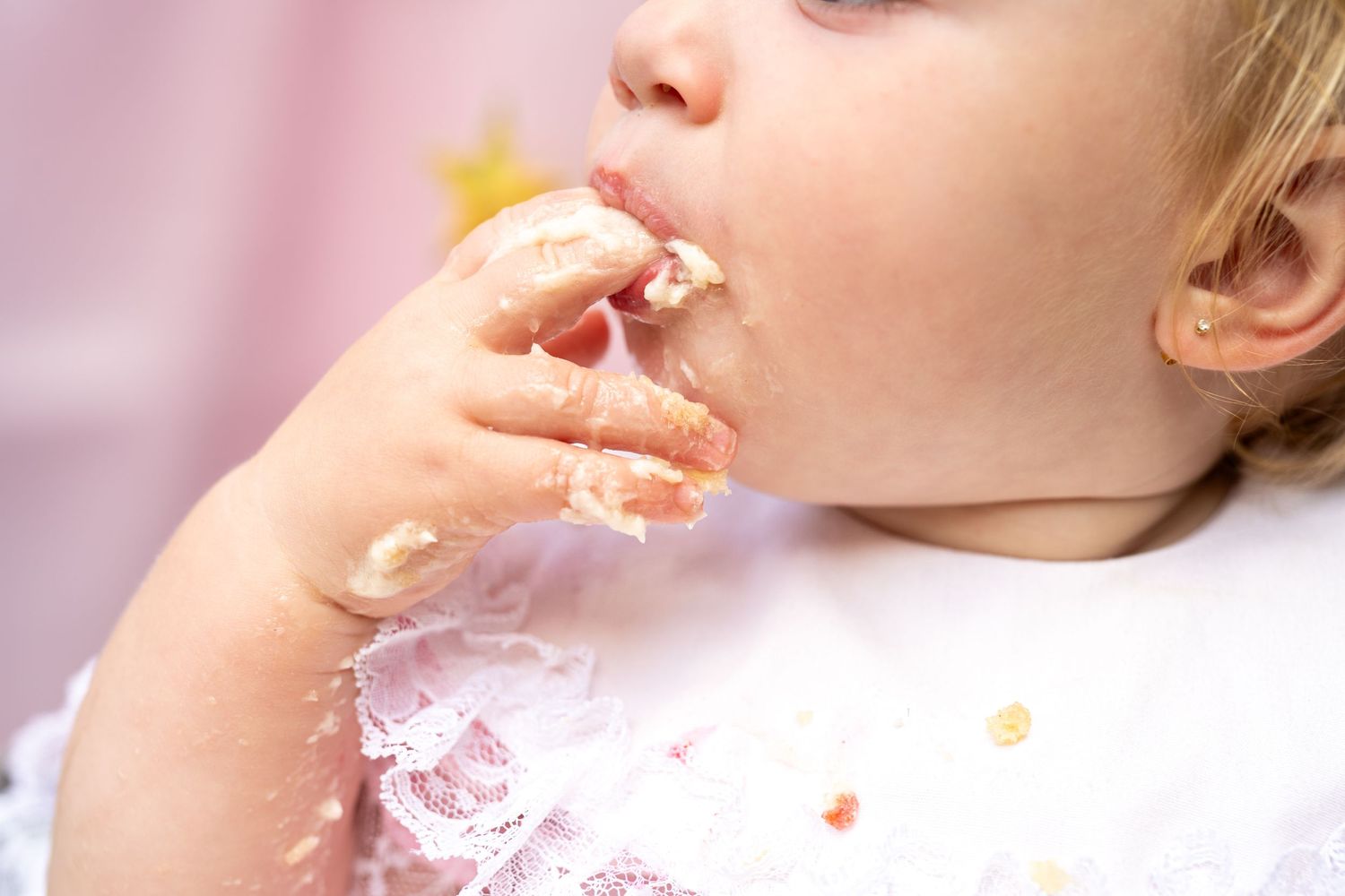 Baby girl with messy hands eating cake during first birthday celebration.
