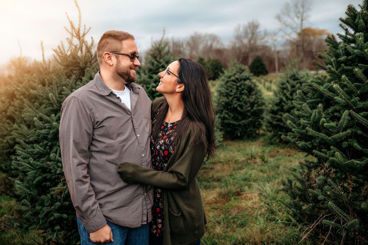 Couple sharing a romantic moment at a Christmas tree farm surrounded by lush green pine trees.