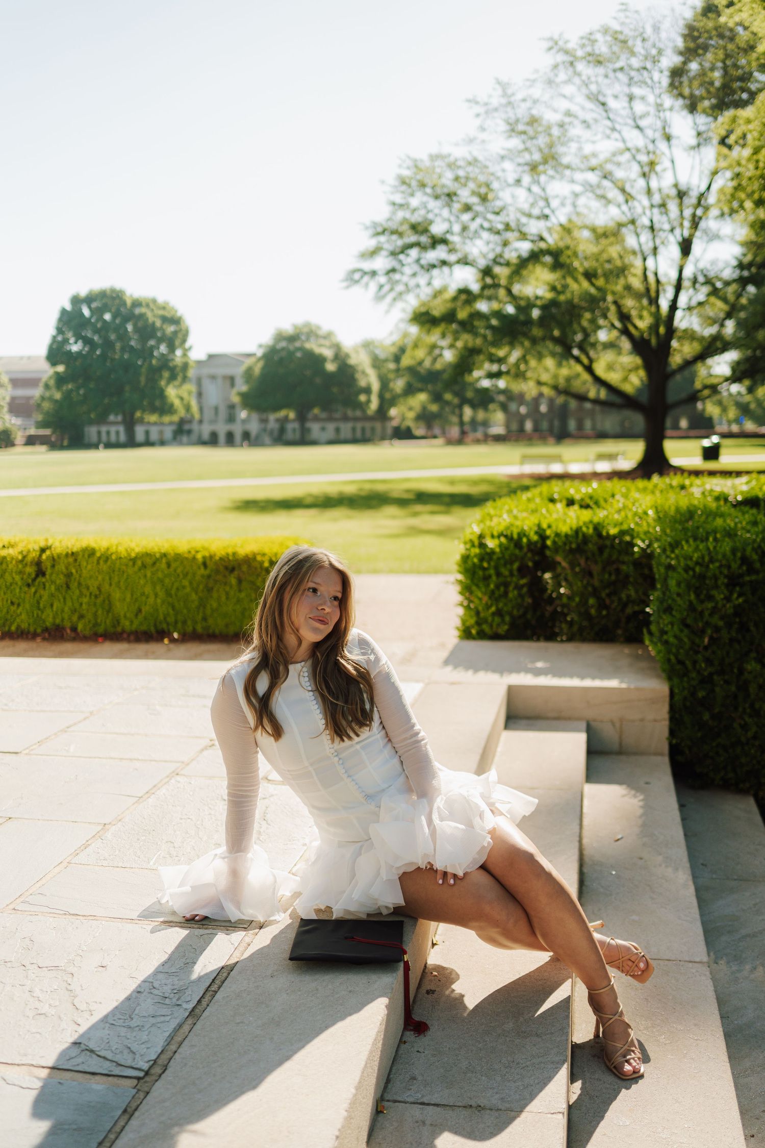 A college senior girl in a white dress sitting on stairs during her senior grad photo session.