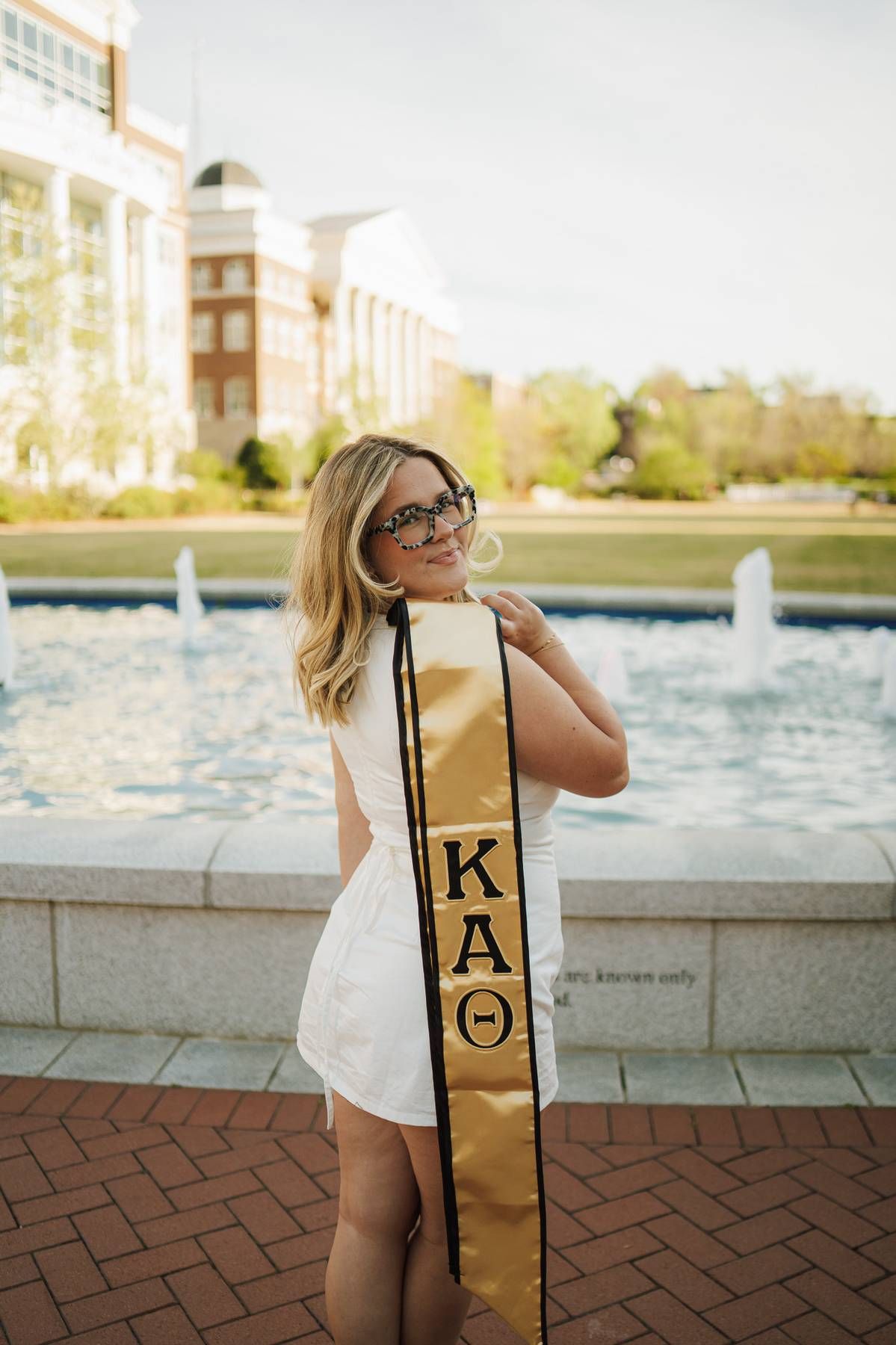 college senior girl wearing a white dress holding her sorority letter sash during her senior photo session.