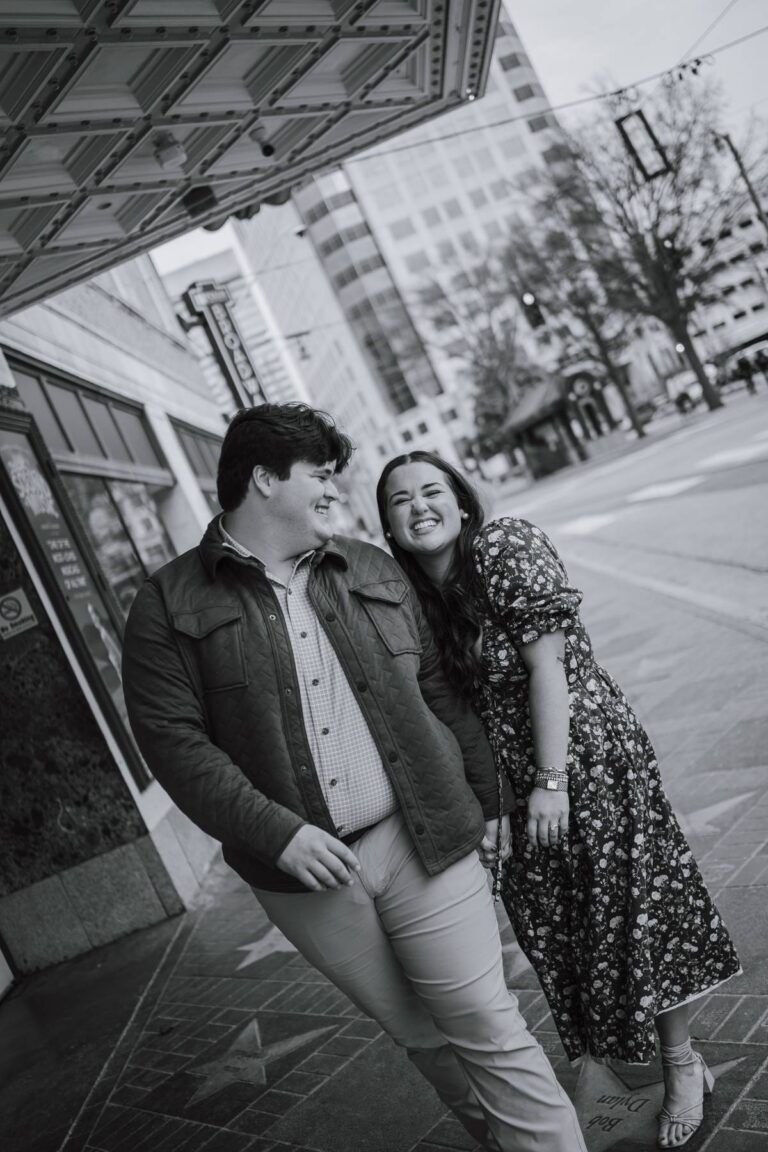 a black and white photo of a engaged couple holding hands and walking in a city