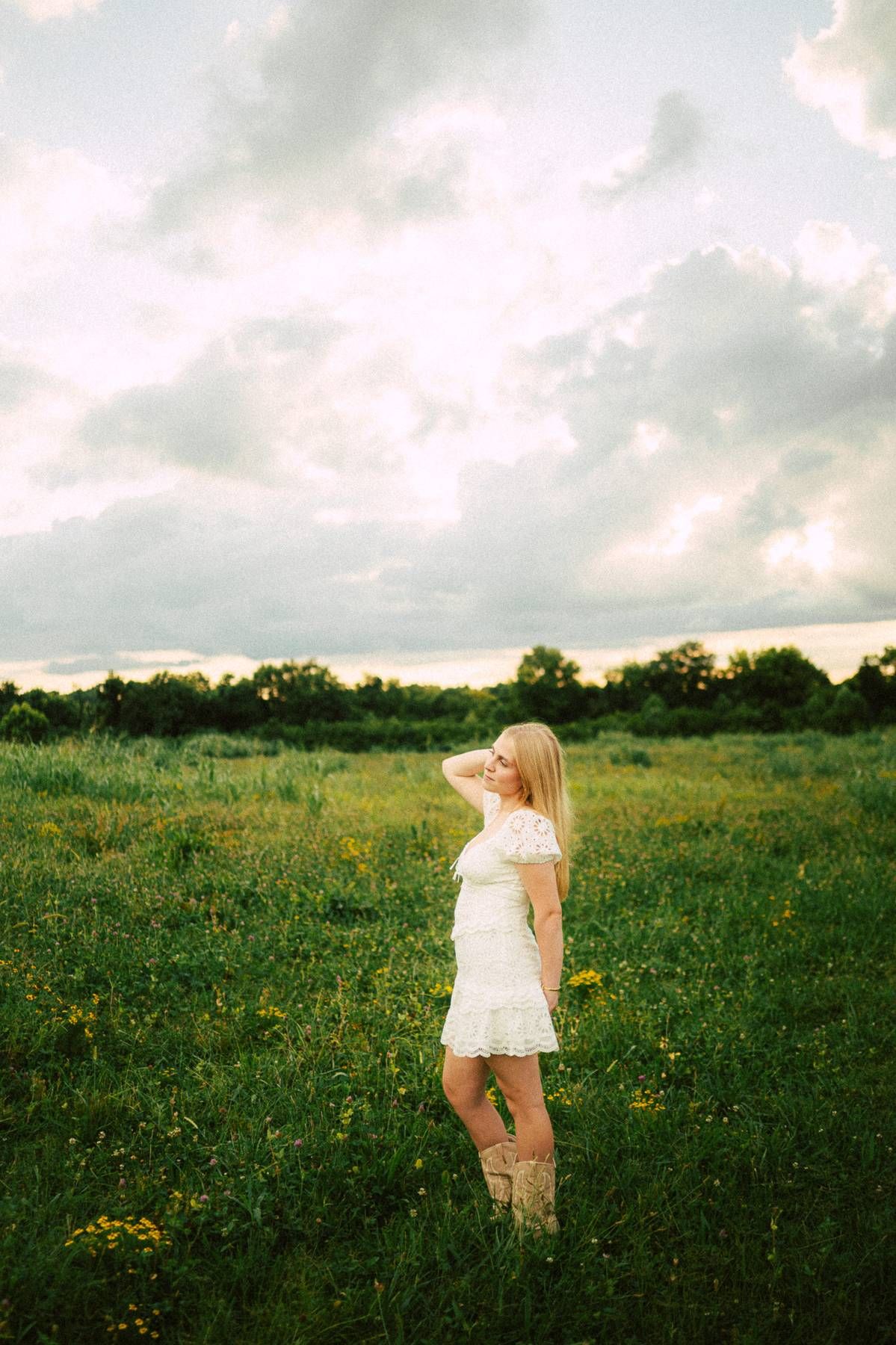 A senior girl in a white dress standing in a grassy field during her grad photo session