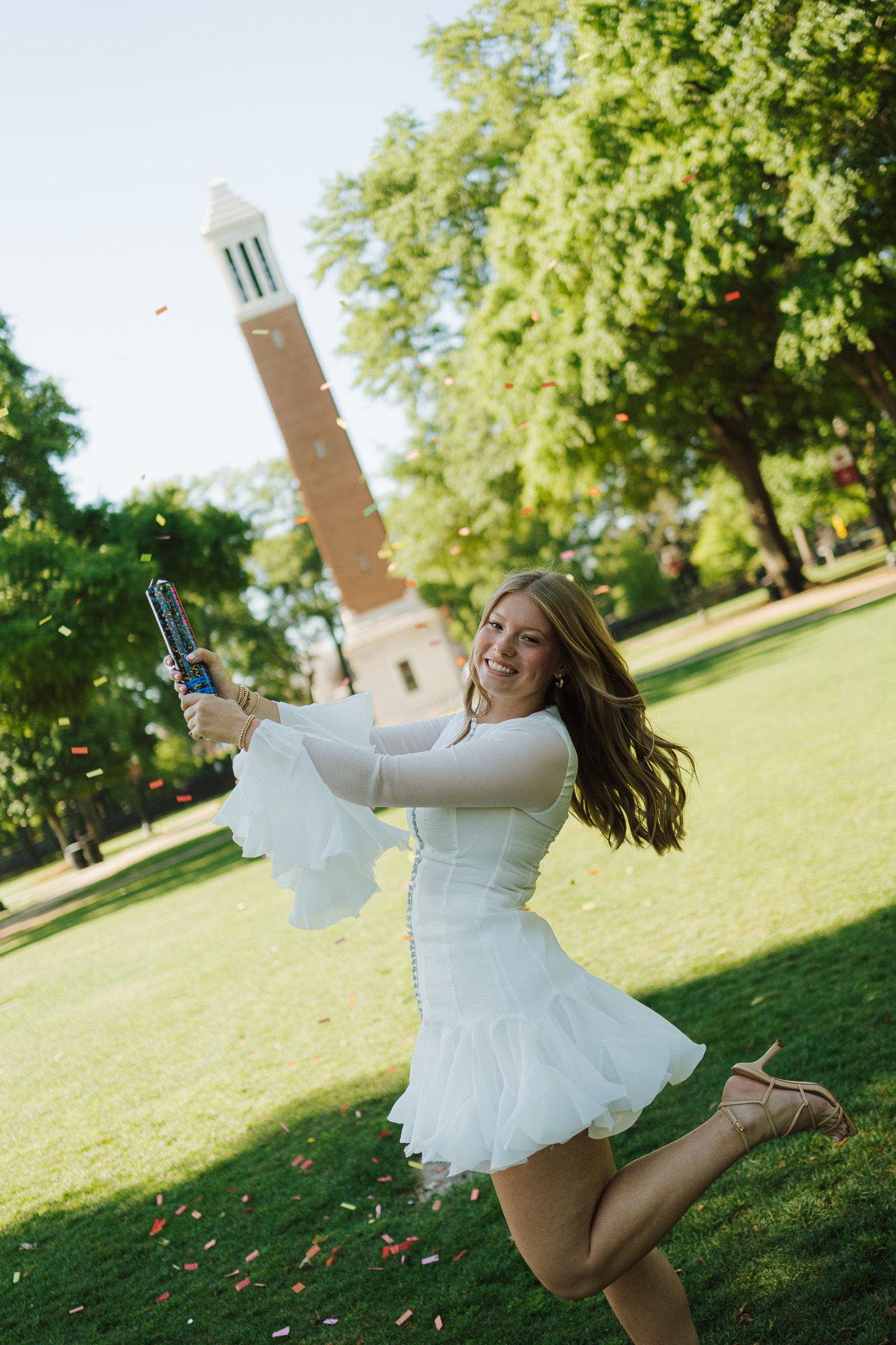 college senior girl wearing white dress popping confetti during her grad photo session.